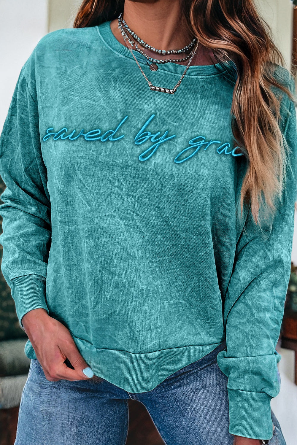 Teal sweatshirt with 'saved by grace' text worn by a person indoors.