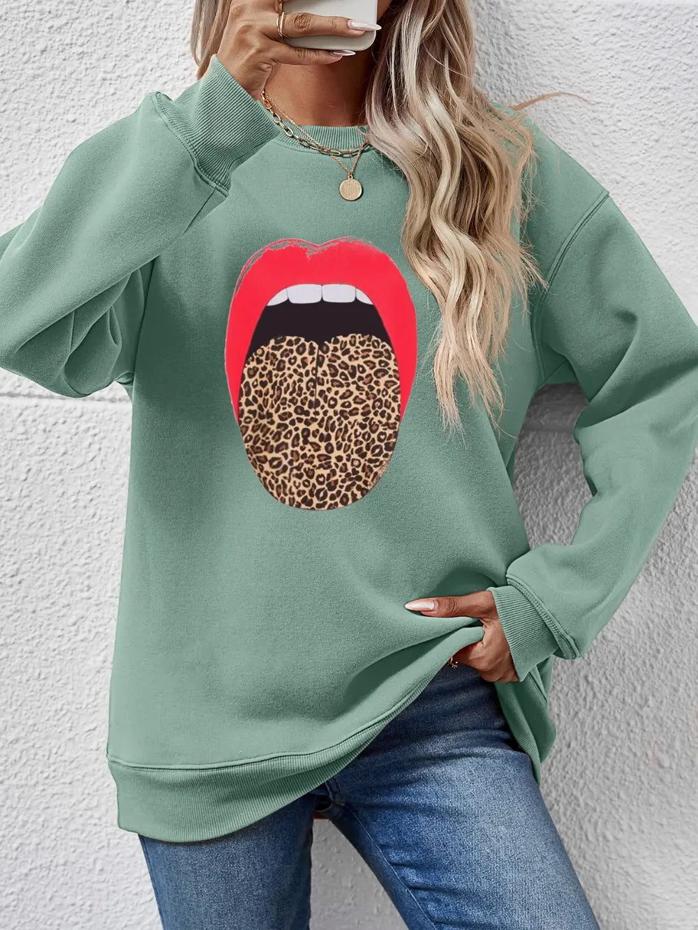 Person wearing a green sweatshirt with a red lip and leopard print design against a white wall.