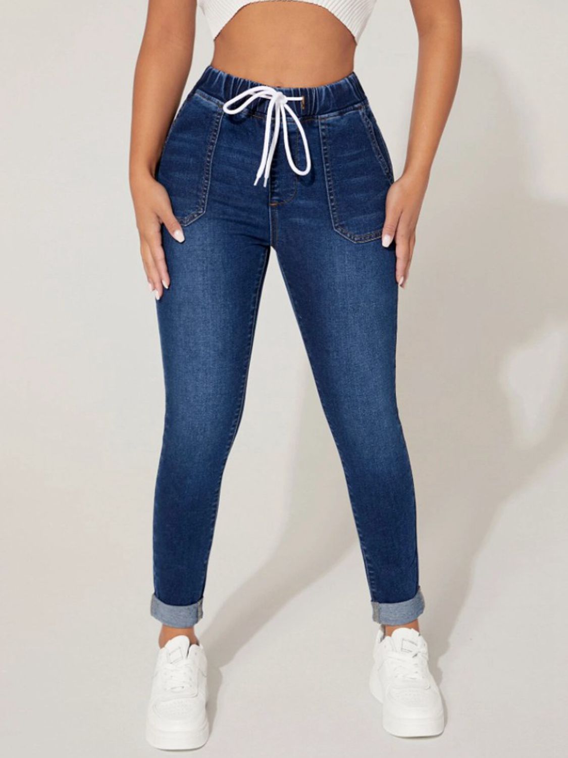 Person wearing blue jeans with a drawstring waist on a plain background