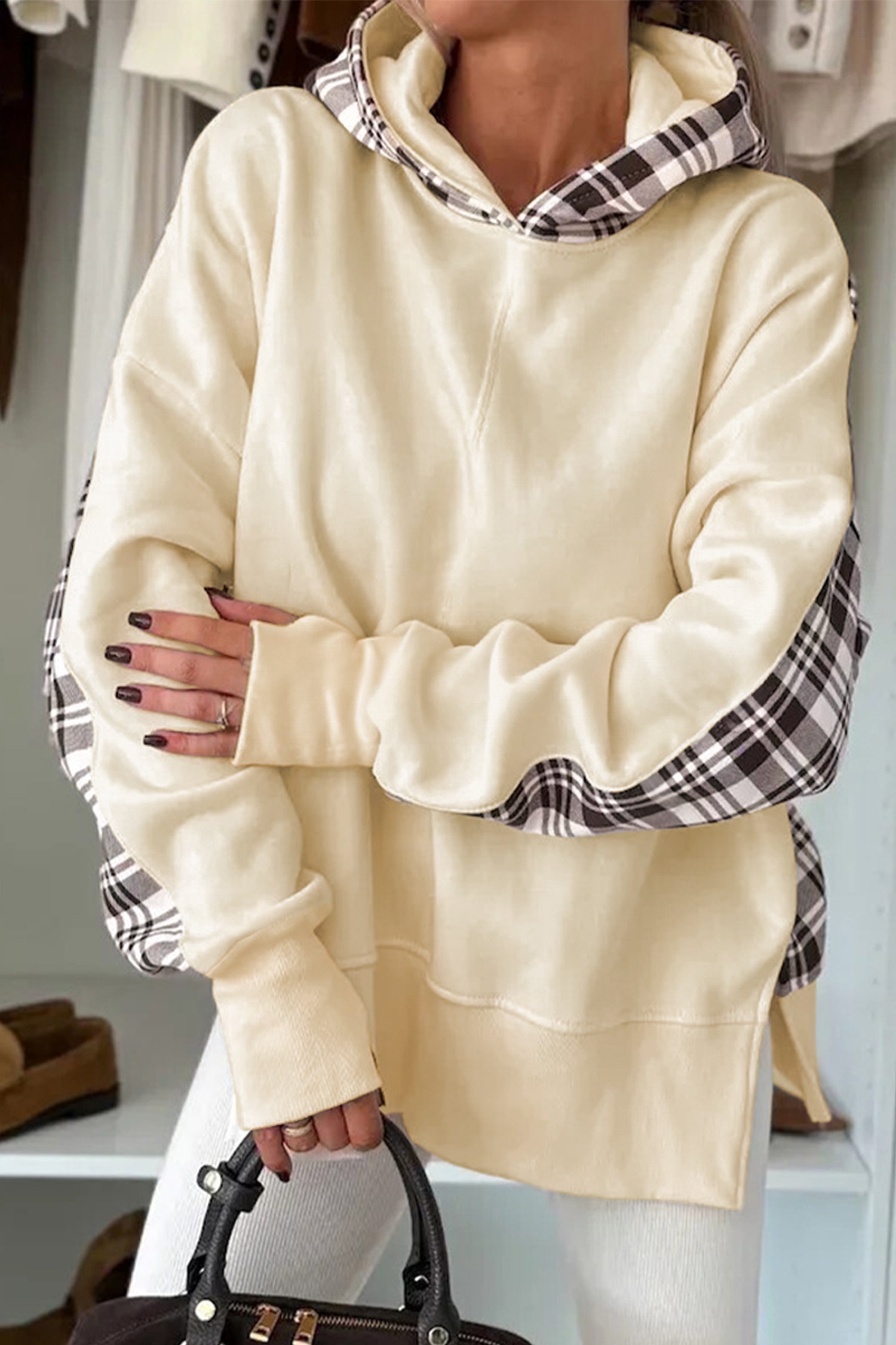 Person wearing a cream-colored hoodie with plaid accents, holding a black handbag.