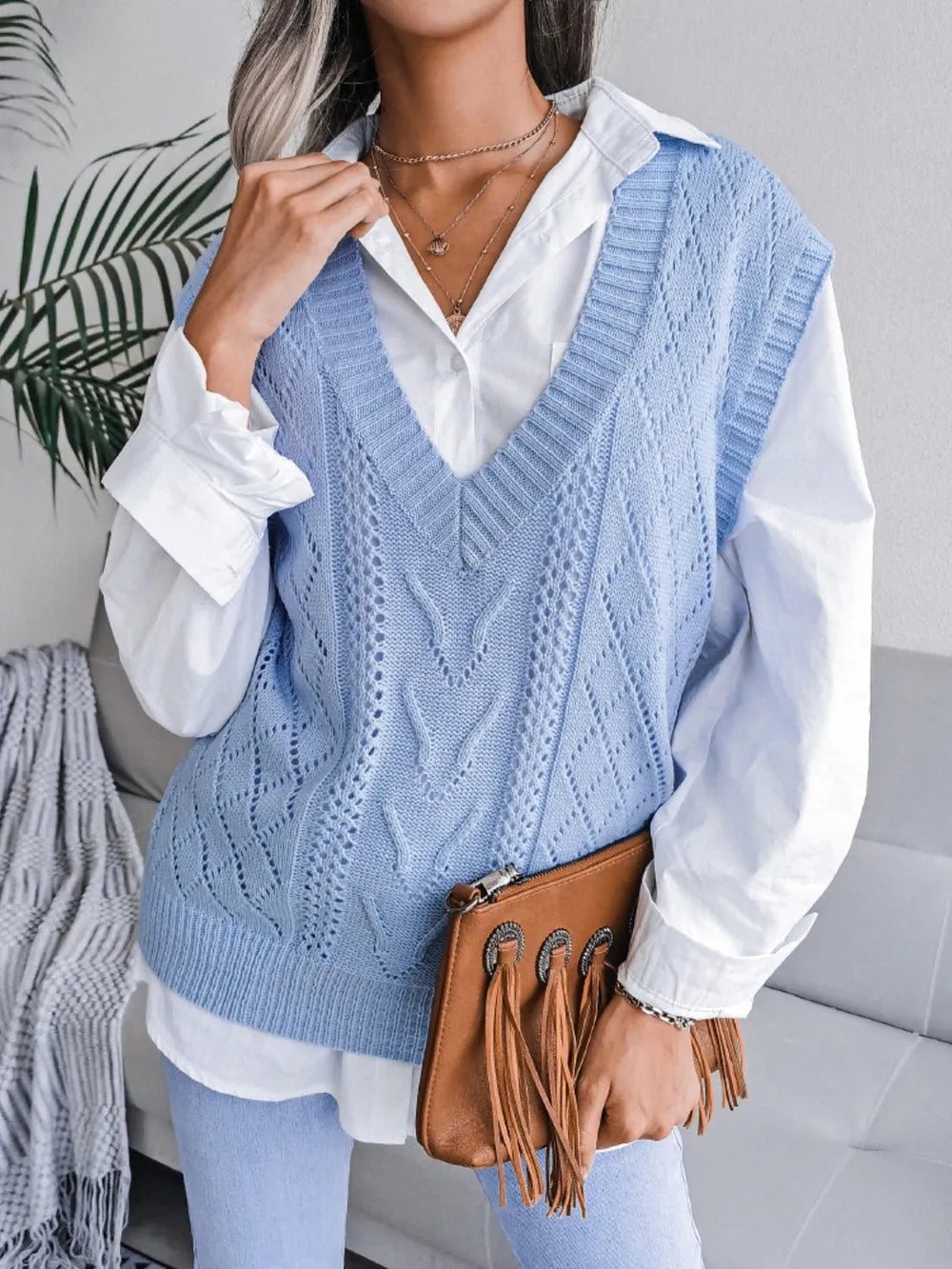 Person wearing a blue knitted vest over a white shirt with a brown handbag.