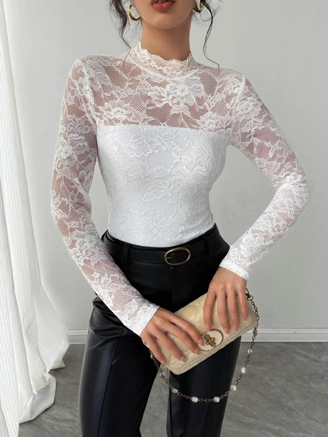 Person wearing a white lace long-sleeve top and black pants, holding a beige clutch.