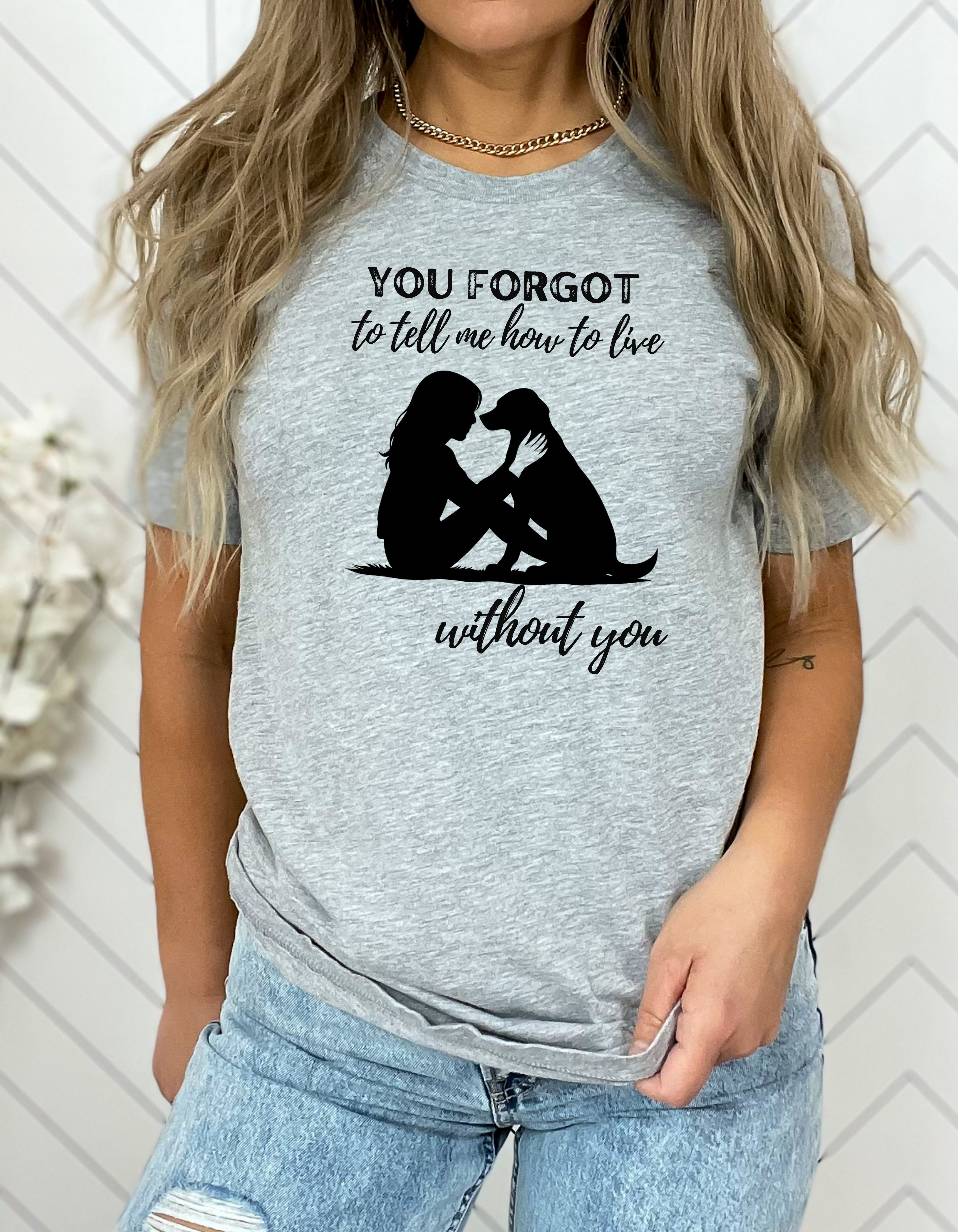 Person wearing a gray t-shirt with a graphic and text, standing against a white wall.