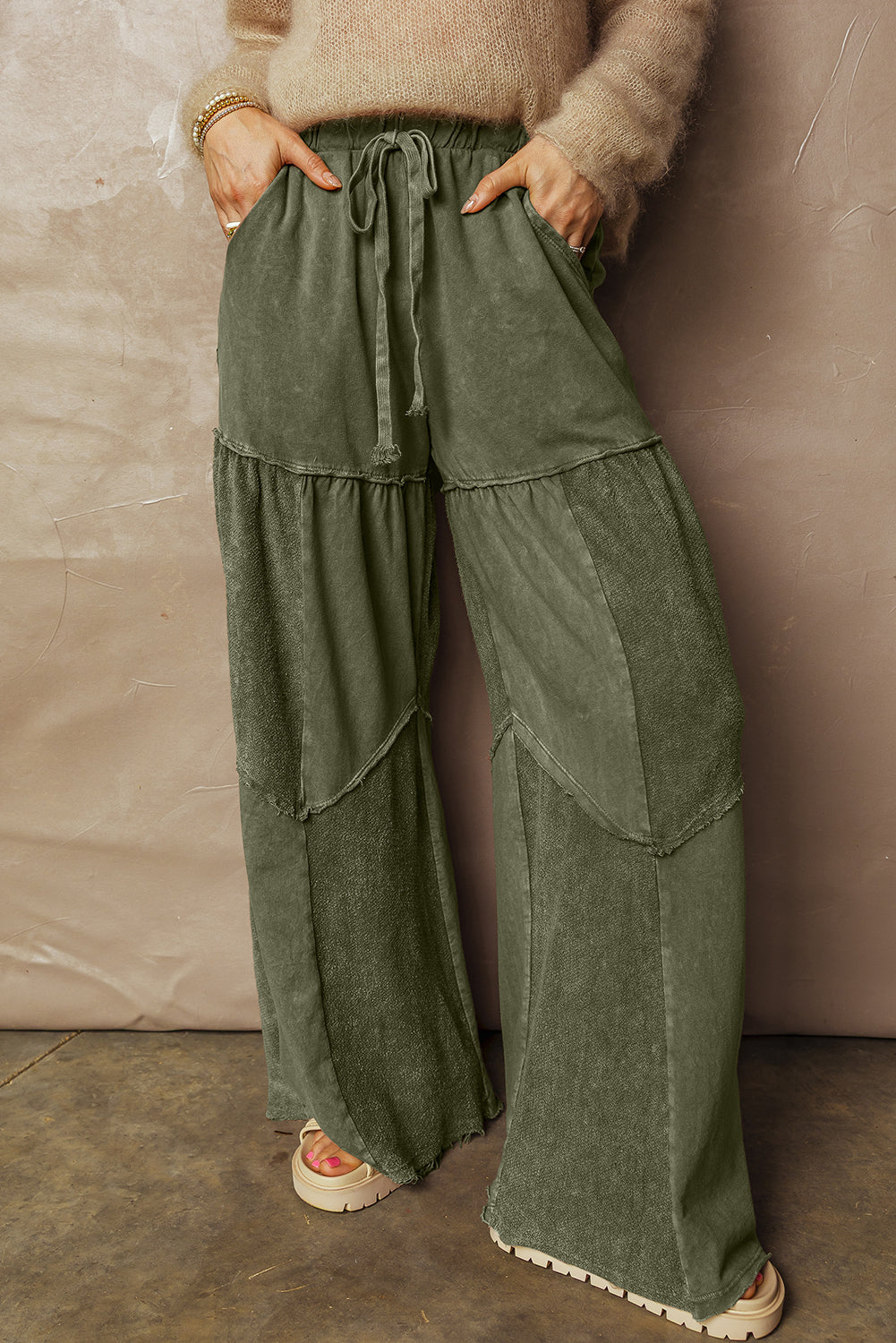 Person wearing green wide-leg pants against a beige wall.