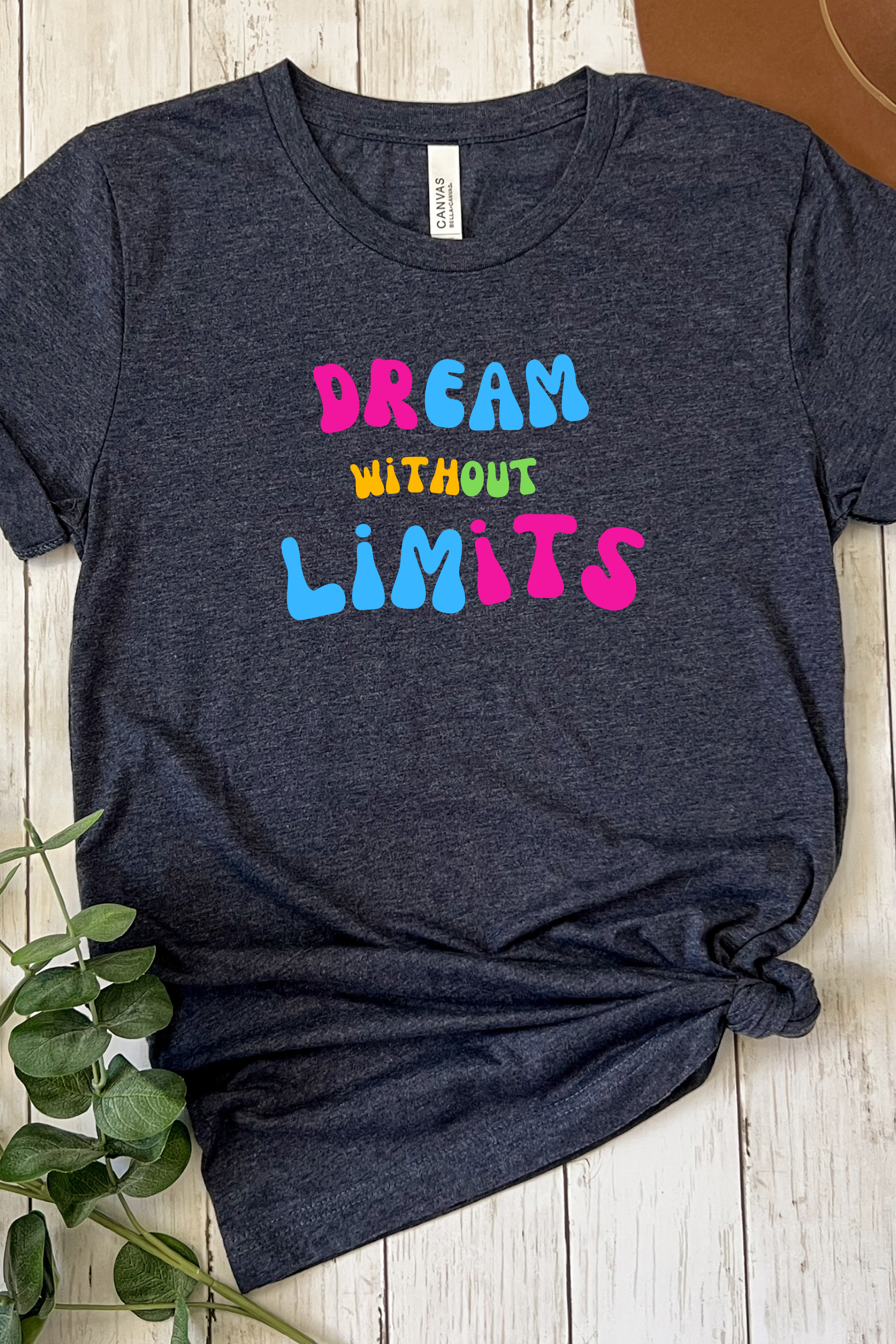 Navy blue t-shirt with 'Dream Without Limits' text on a wooden surface